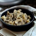 Cooked stroganoff in black bowl with tan napkin.