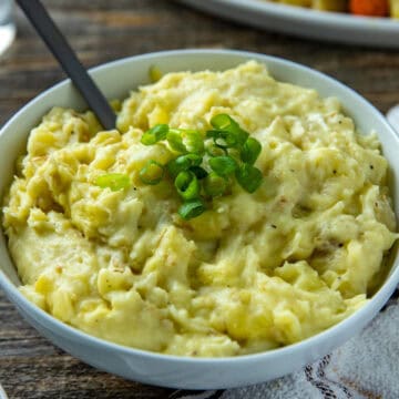 Mashed potatoes in white bowl with sliced green onions as a garnish on top.