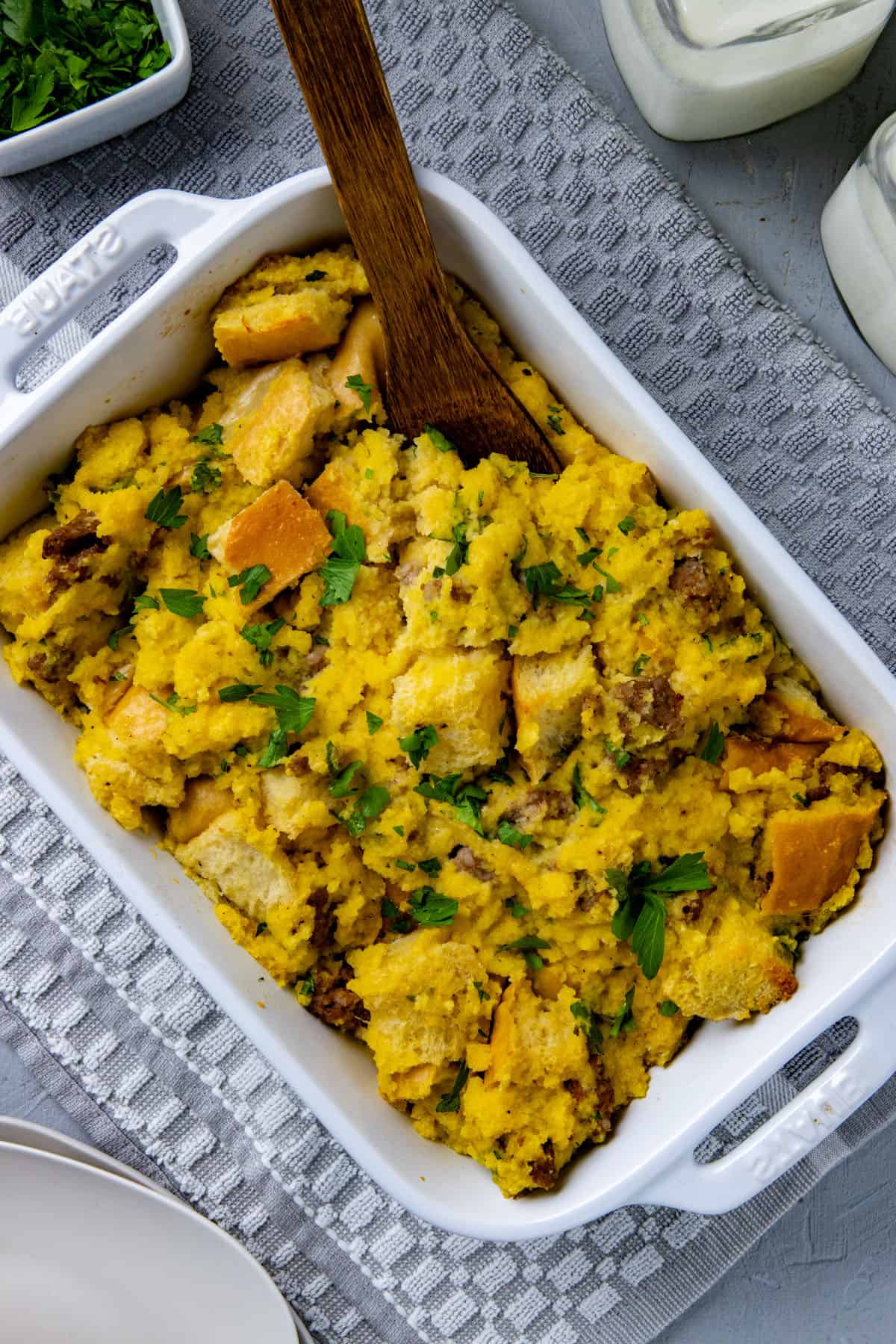 Baked stuffing in a white casserole dish with wooden spoon digging in.