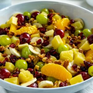 Fruit salad mixed with honey lime dressing in a white bowl.