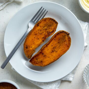 Two roasted sweet potato halves on a round white plate with a fork.