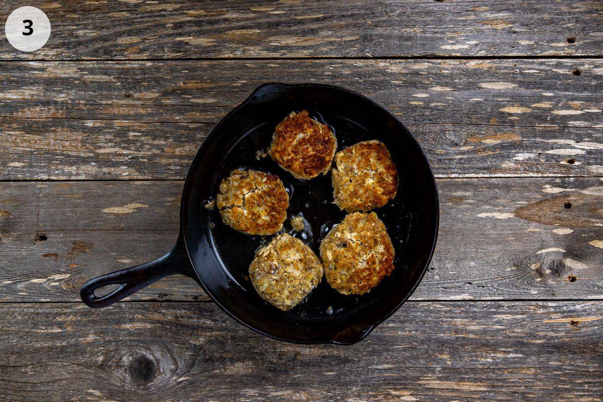 Five cooked patties in a cast iron skillet.