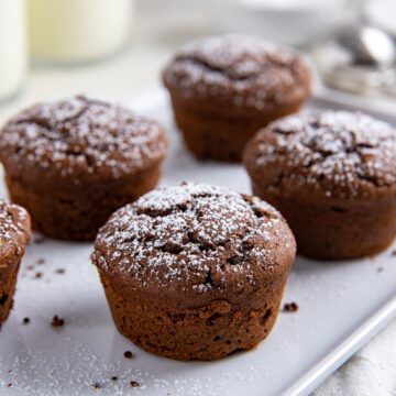 Baked chocolate muffins on a white serving platter.