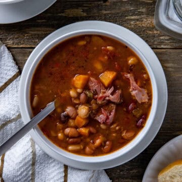 Cooked bean soup in a white bowl with French bread on the side.