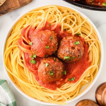 Three cooked venison meatballs with marinara sauce on top of cooked spaghetti.