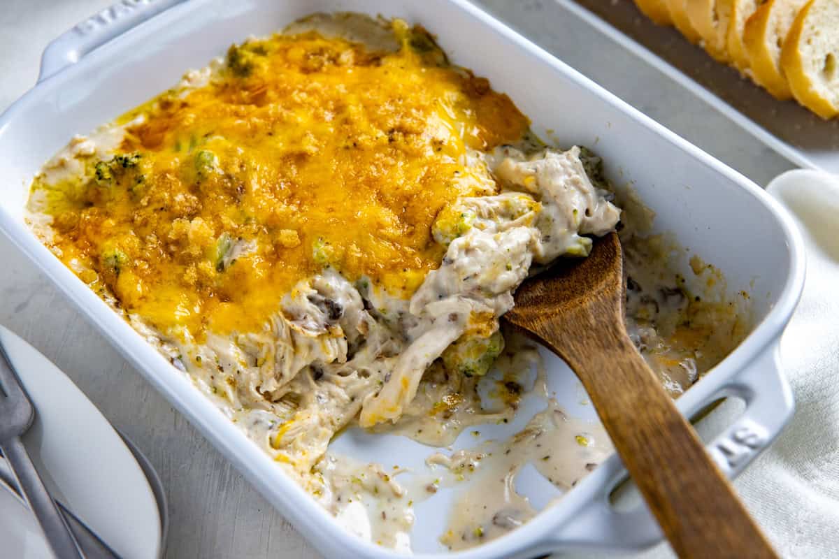Baked casserole in white casserole dish with wooden spoon removing a portion.
