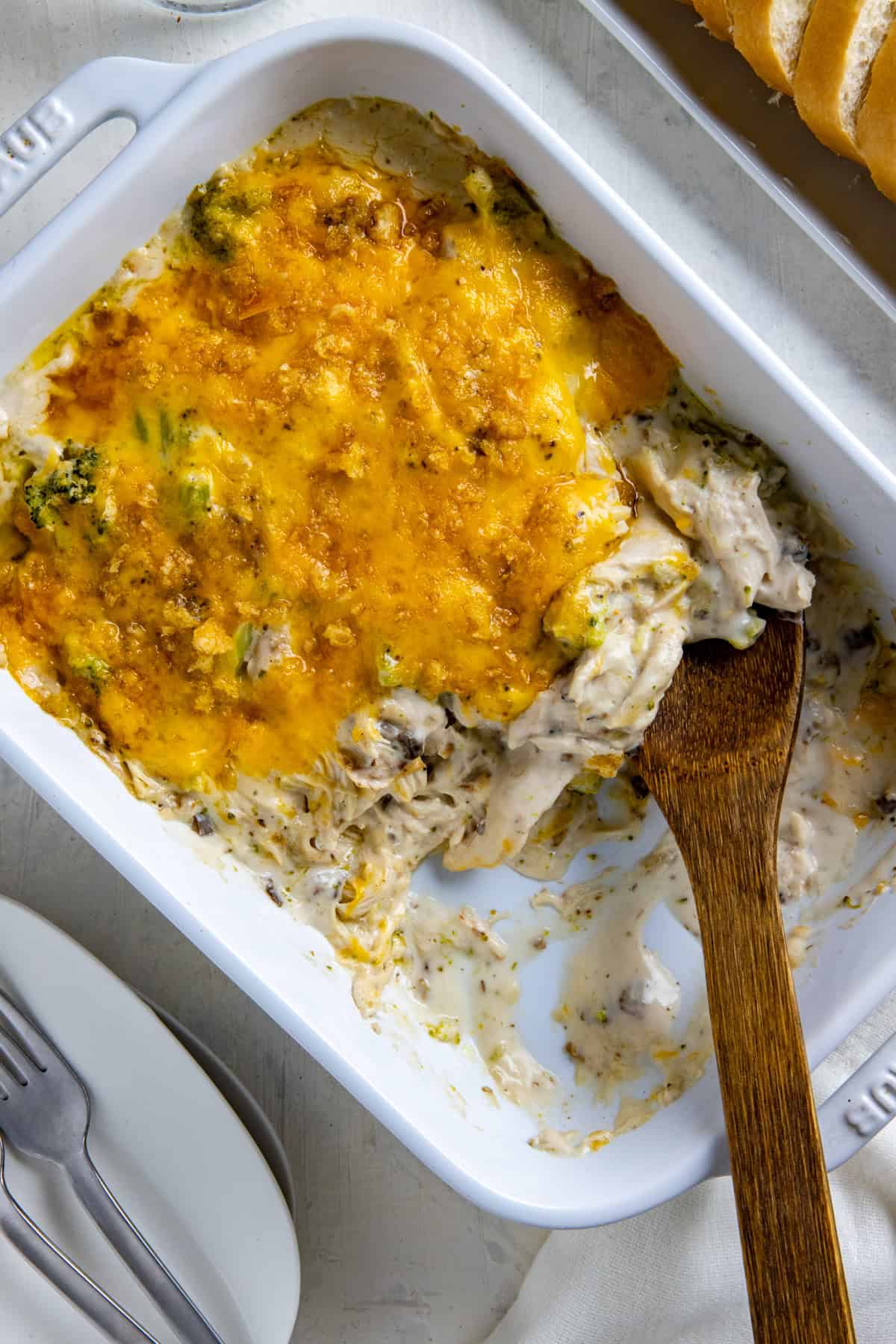 Baked casserole in white casserole dish with wooden spoon removing a portion.