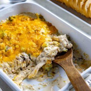 Baked casserole in white baking dish with wooden spoon removing a serving.