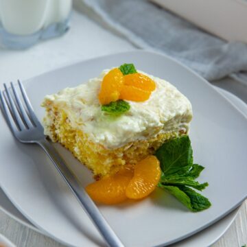 A slice of cake topped with two of mandarin orange segments and mint leaves on a square white plate with a fork.