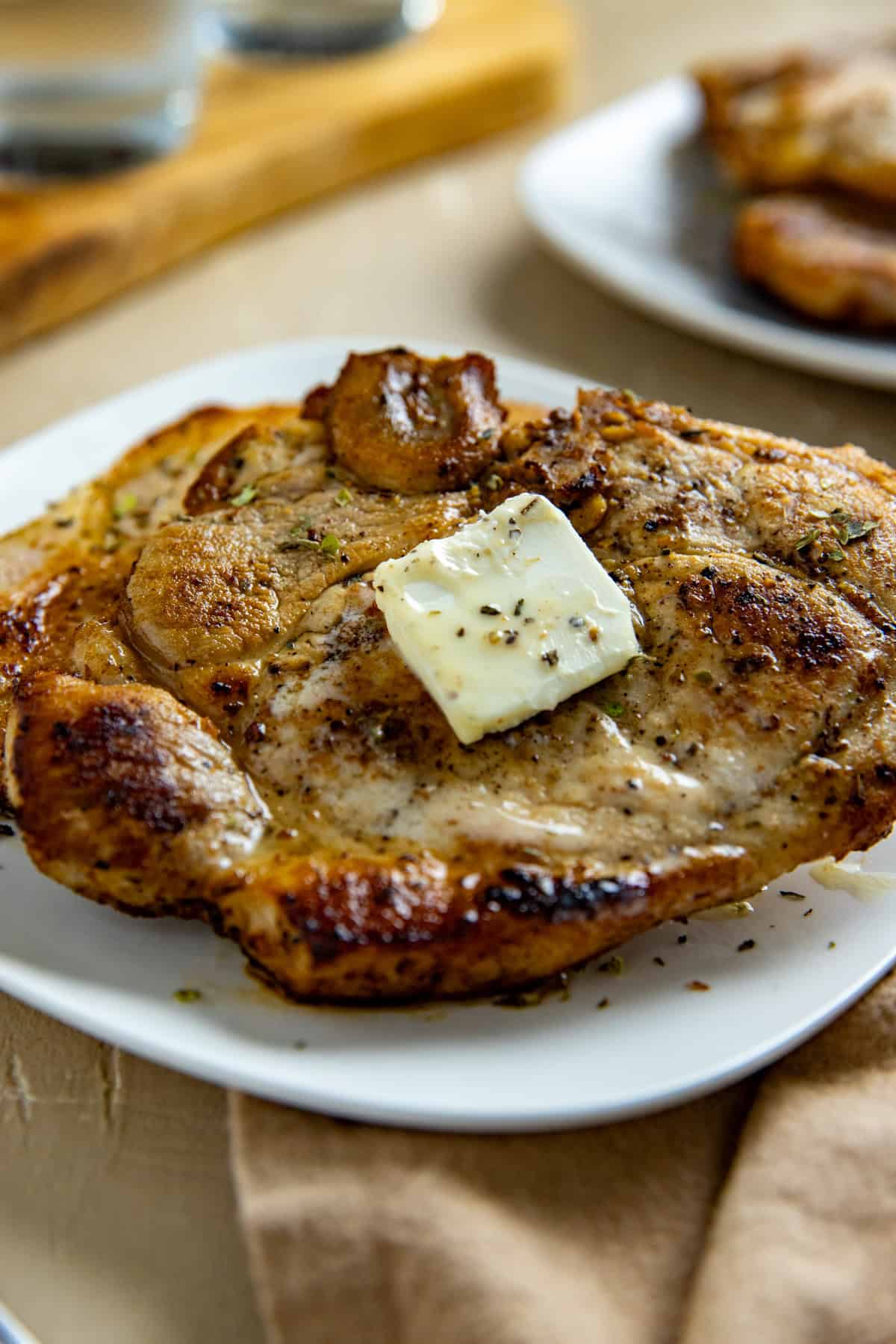 One cooked and seasoned pork chop with a pat of butter on top on a white serving plate.