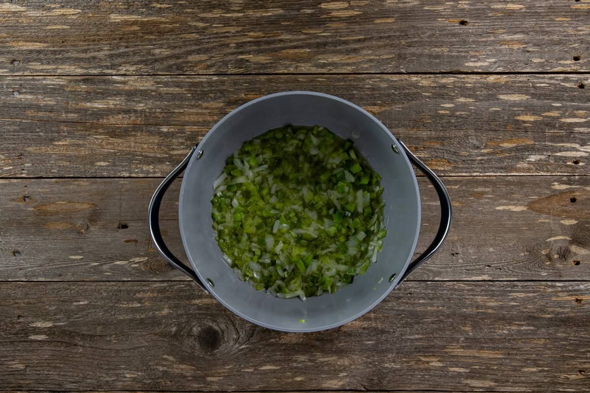 Chopped onion, bell pepper, and celery cooking in a pot with butter,