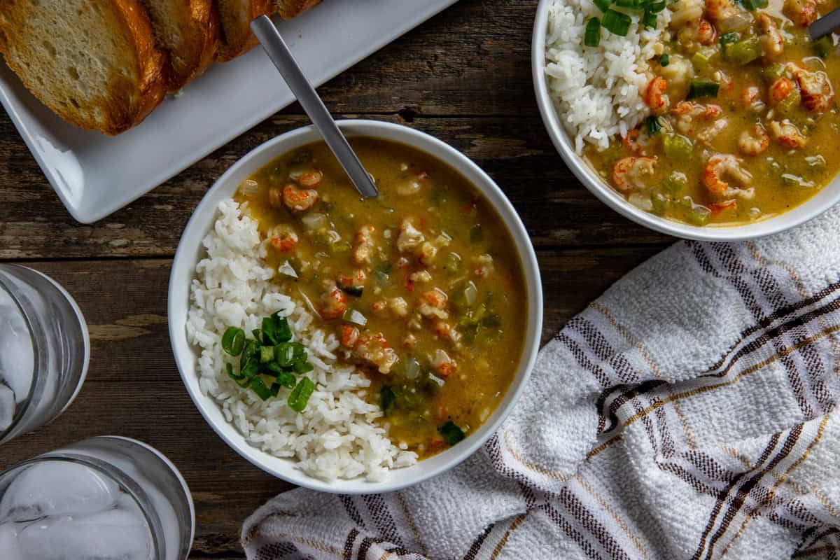 Two bowls of etouffee with white rice. Sliced green onions for garnish. With sliced, toasted French bread in the background.