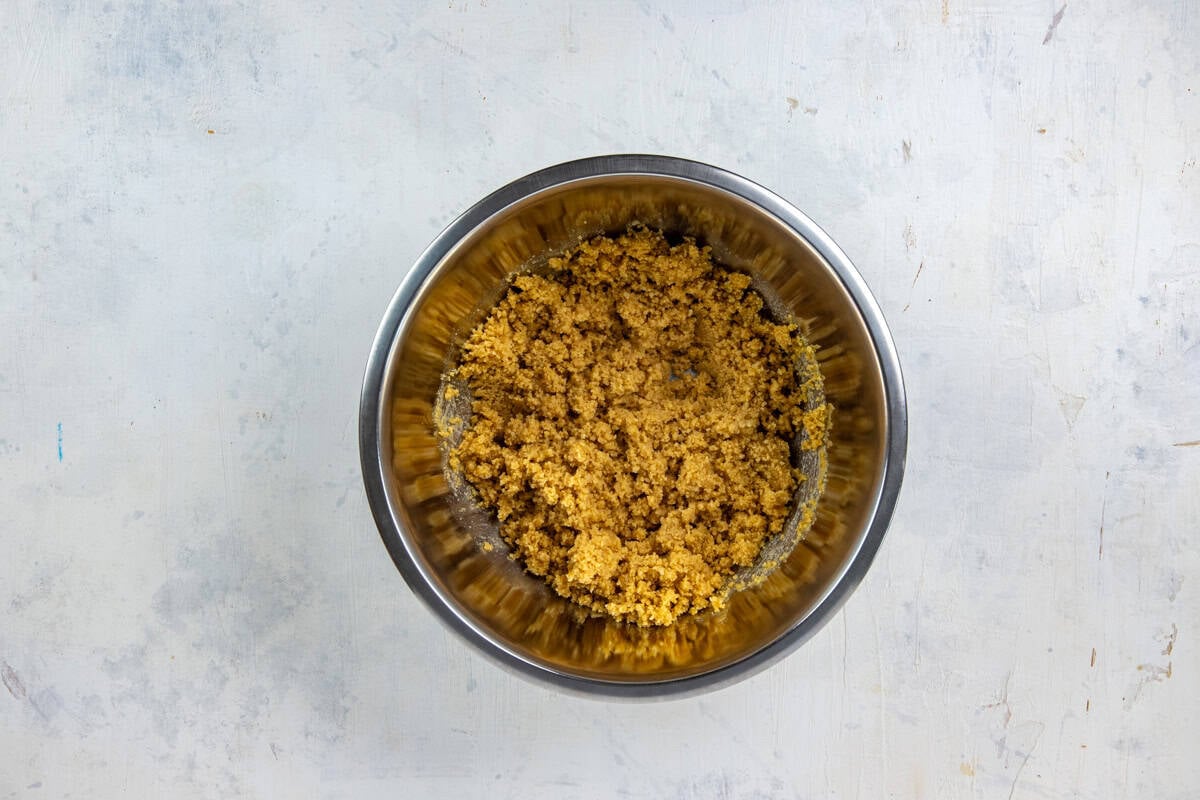 Stainless steel mixing bowl with crushed shortbread cookies and melted butter all mixed up.