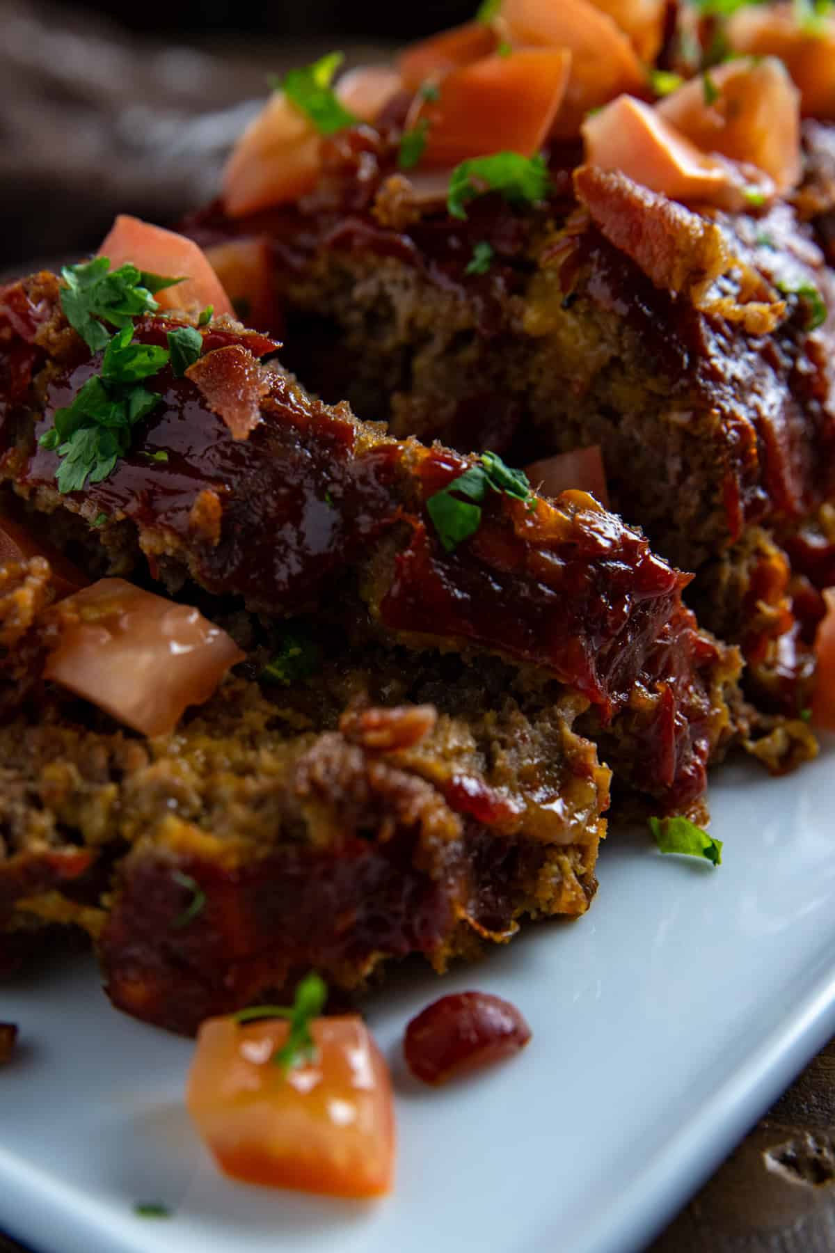 Baked and sliced meatloaf topped with chopped tomatoes and crispy bacon pieces.