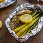 Baked chicken breast with asparagus spears, rosemary sprig, and lemon slice in a foil packet.