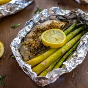 Baked chicken breast with asparagus spears, rosemary sprig, and lemon slice in a foil packet.