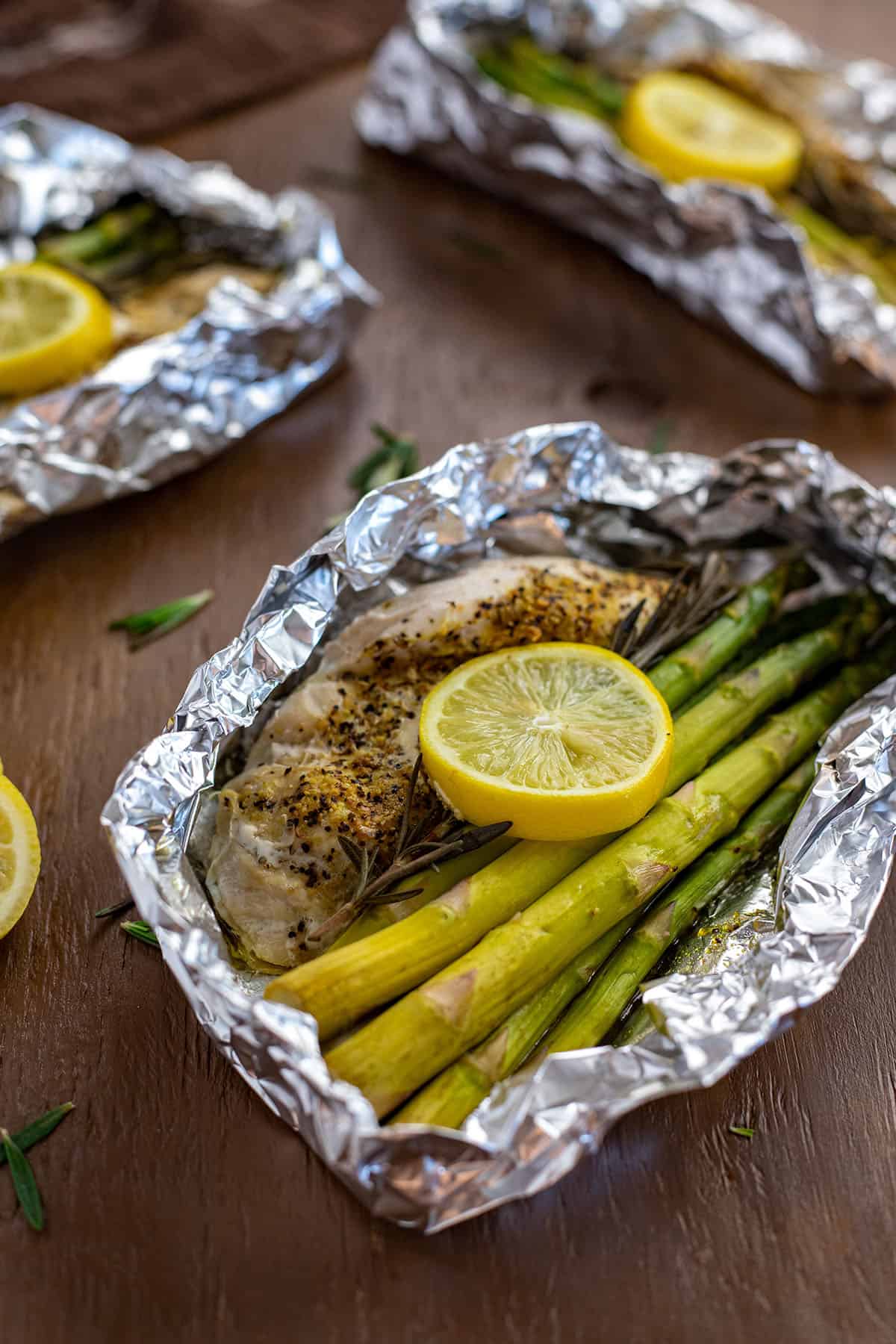 Lemon Pepper Chicken with rosemary and asparagus inside foil packet with lemon slices on top.