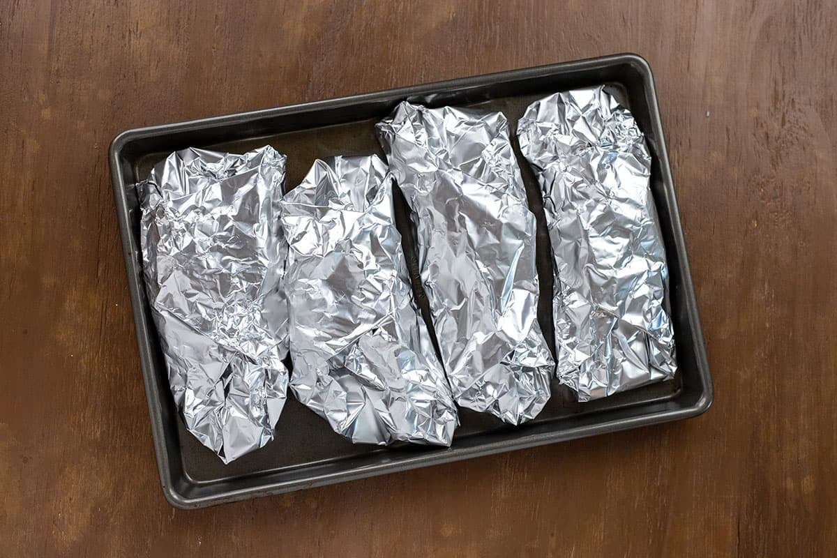 Four foil wrapped chicken breasts on baking pan.