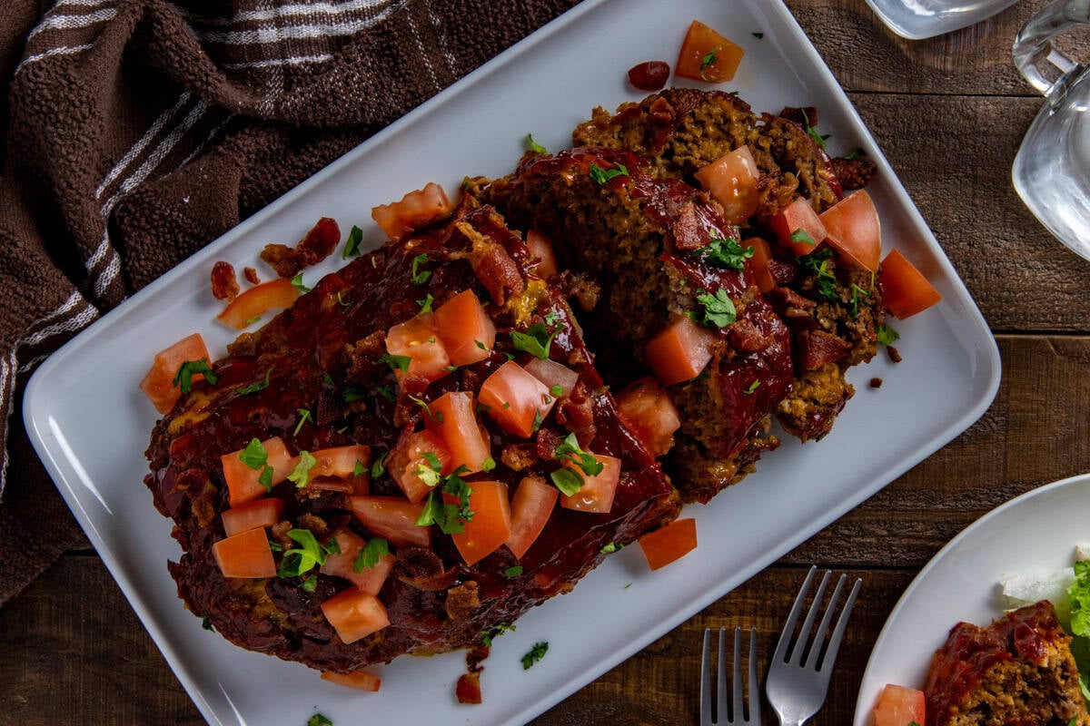 Baked and sliced meatloaf topped with chopped tomatoes and crispy bacon pieces.