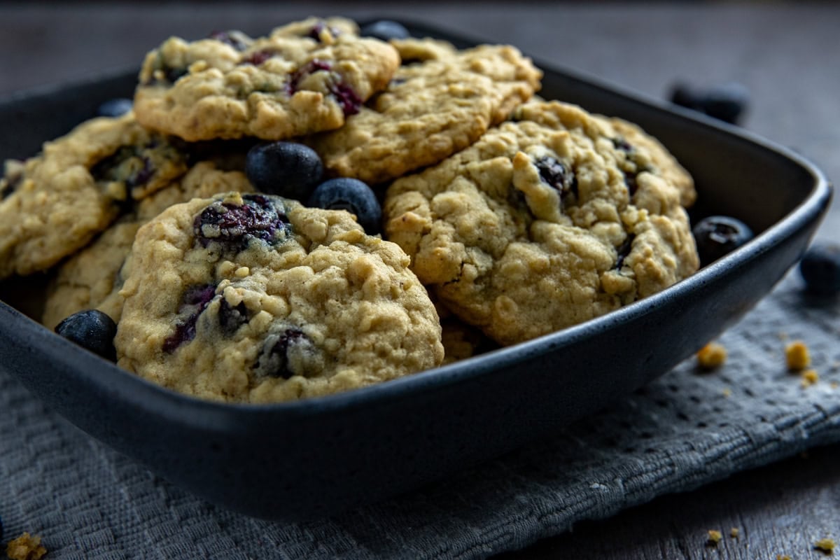 Baked cookies piled high in a square black bowl on a gray napkin.