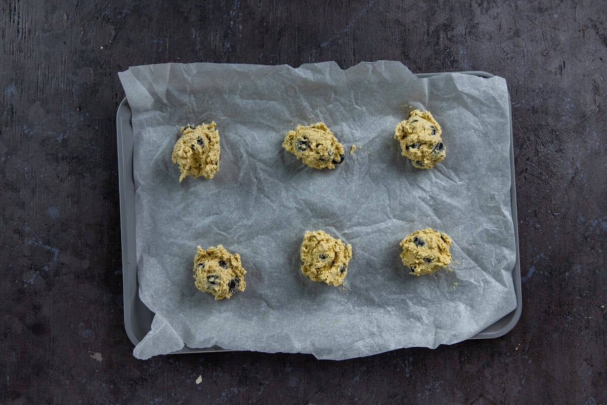 Scoops of raw cookie dough on parchment paper-lined cookie sheet.