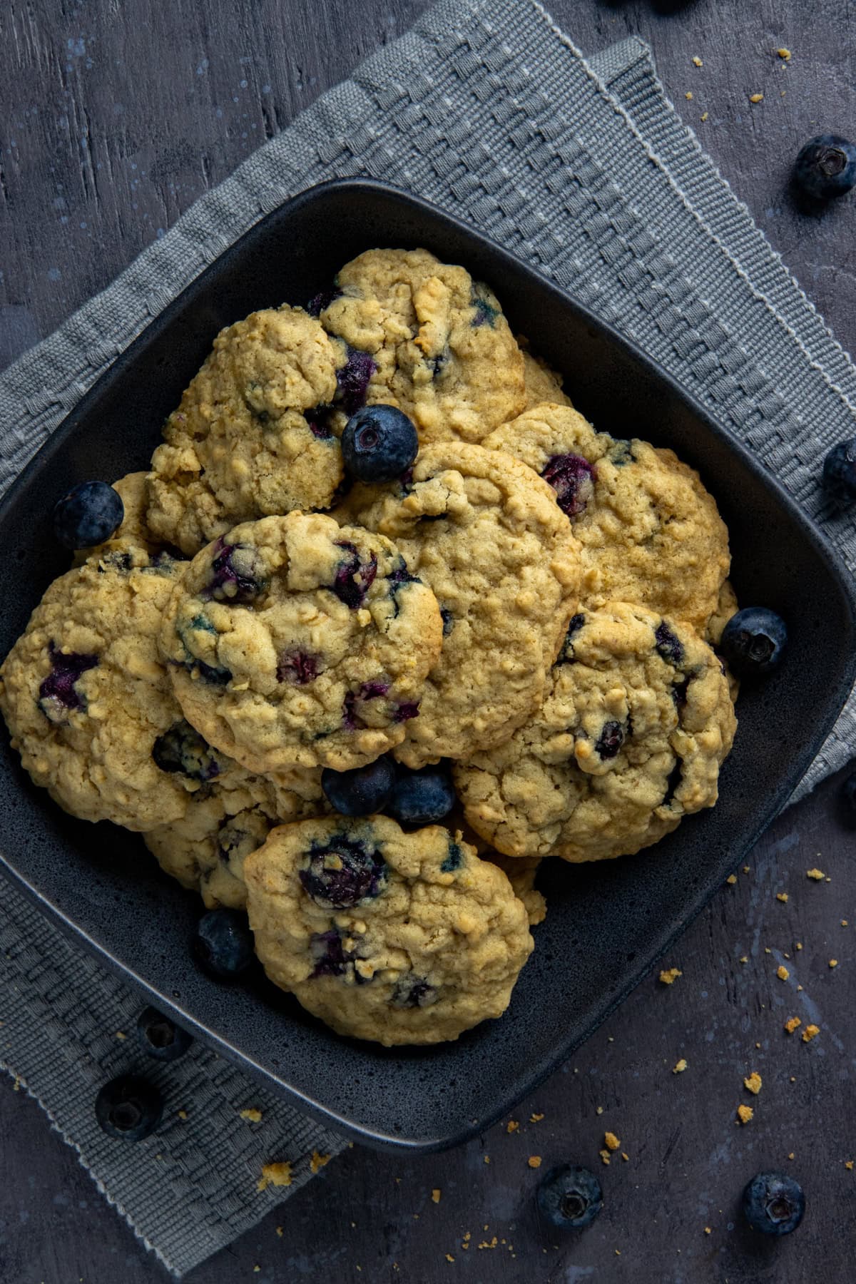 Baked cookies piled high in a square black bowl on a gray napkin.