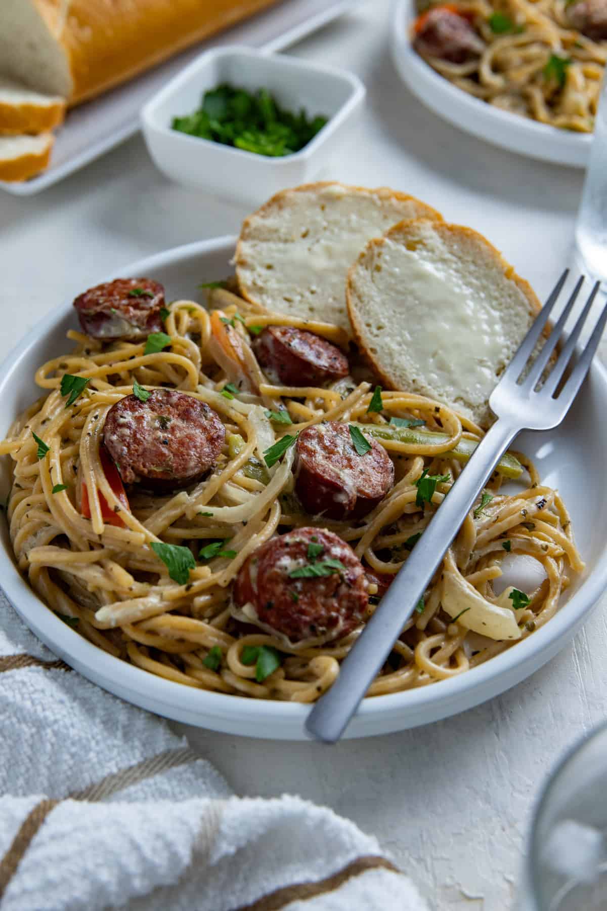 Cooked cajun sausage spaghetti on white plate with a fork and two slices of buttered French bread on the side.