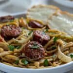 Cooked Cajun spaghetti on white plate with two slices of buttered French bread on the side.