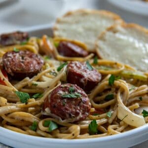 Cooked Cajun spaghetti on white plate with two slices of buttered French bread on the side.