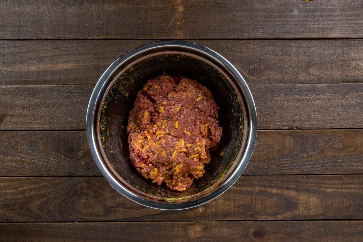 Ground beef, bacon, cheese, and bread crumbs blended into the egg mixture in the mixing bowl.