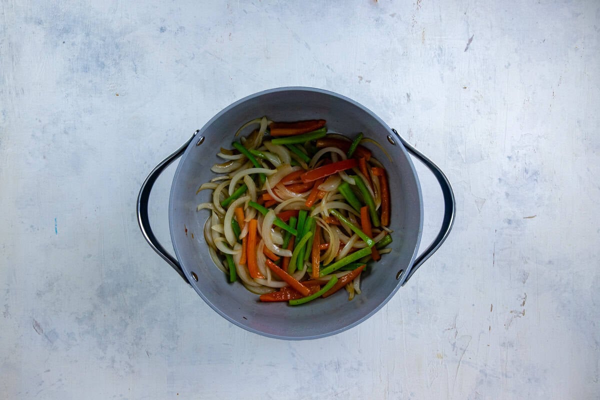 Sliced onions and bell peppers sauteed in a pot.