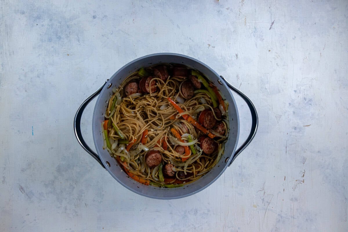 Sausage, onions, and peppers in the pot with broth, seasonings, and raw spaghetti.