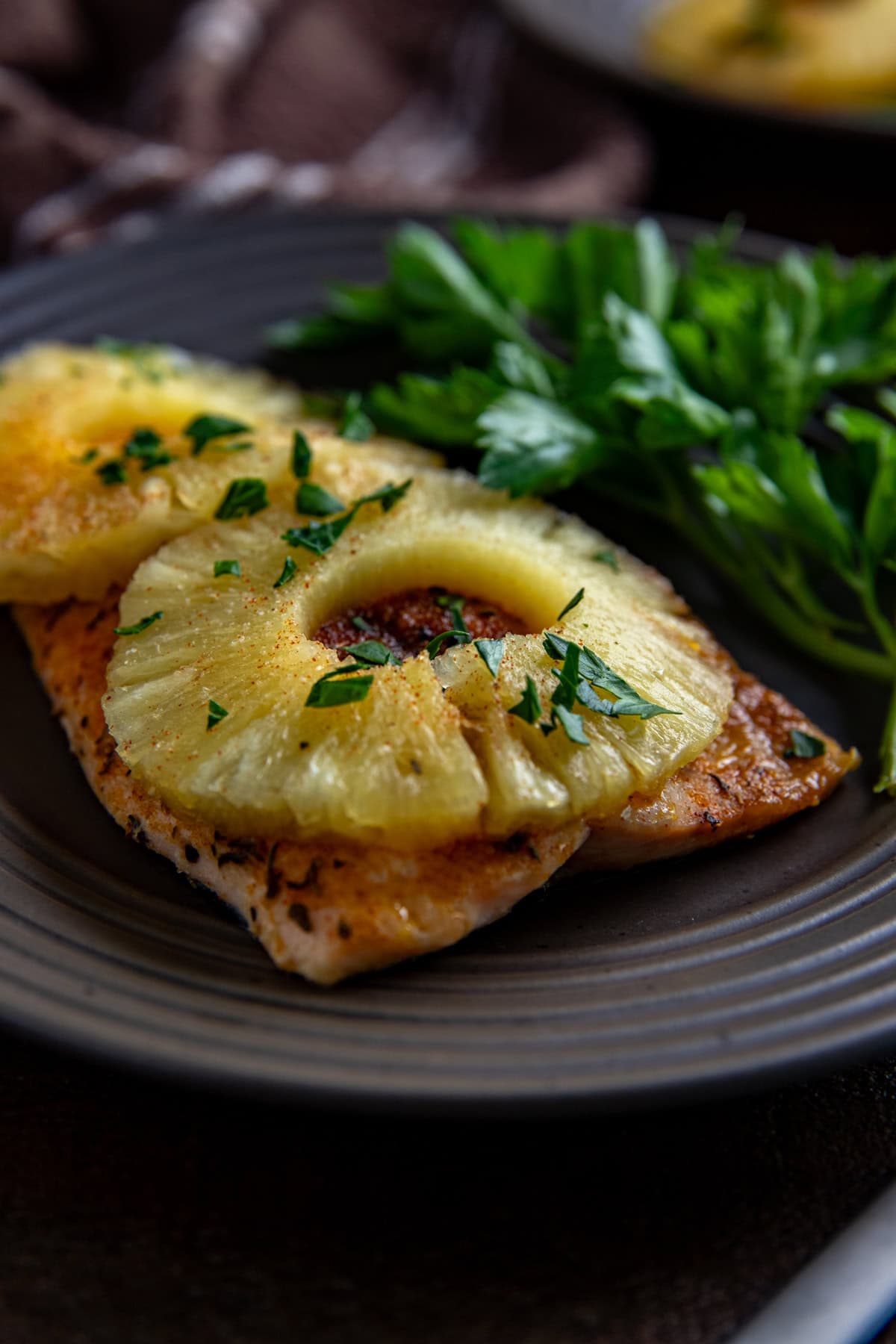 One baked salmon fillet topped with two pineapple rings and sprinkled with fresh cut parsley.