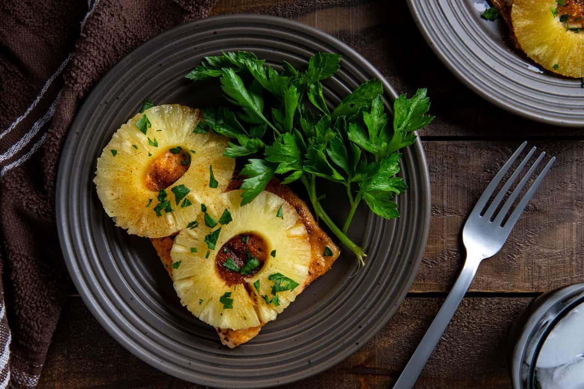 Overhead view of a plated baked salmon fillet with pineapple rings on top.