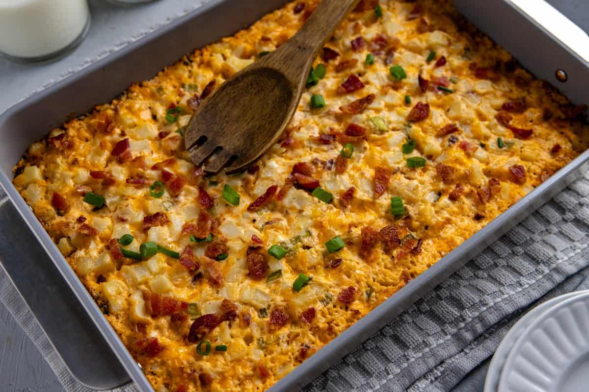 Baked potato casserole in the casserole dish with wooden serving spoon resting on top.