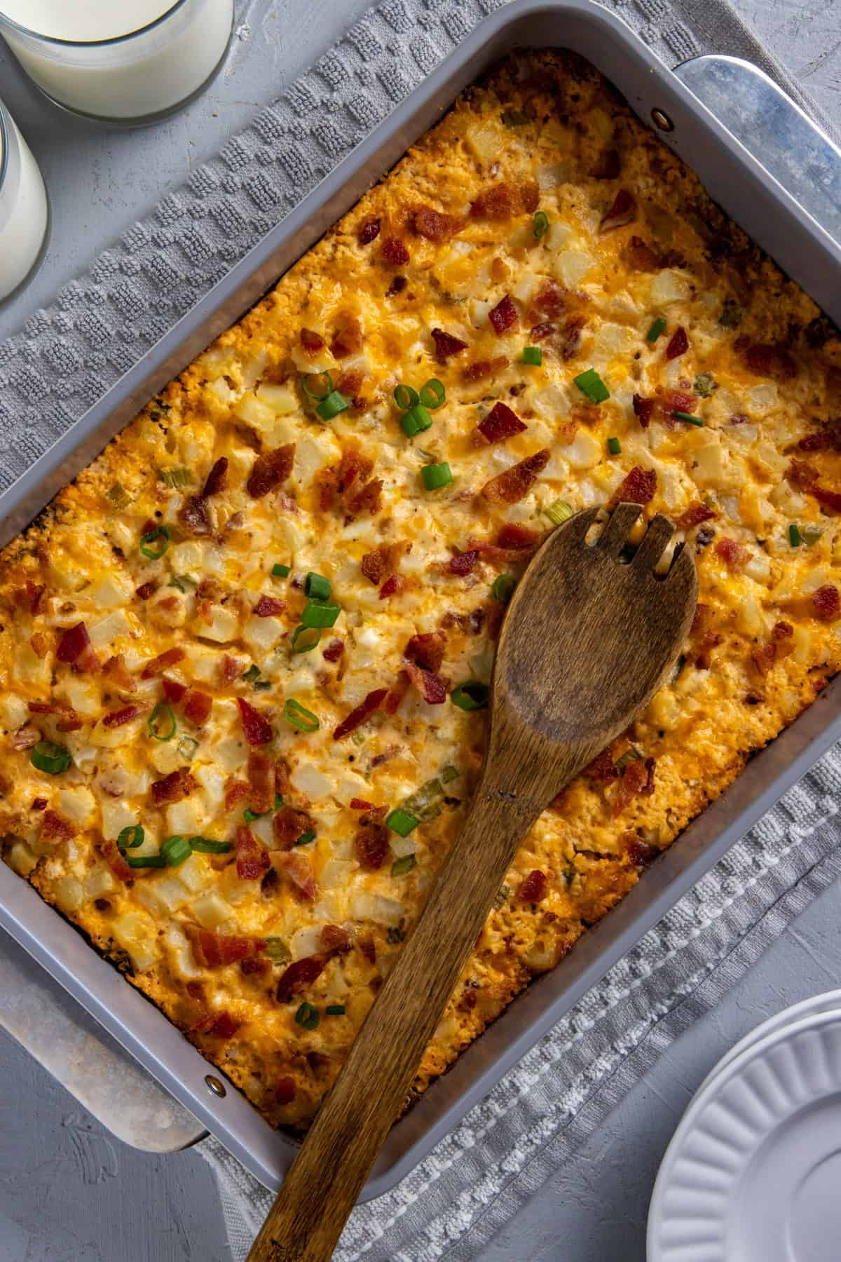 Baked hash brown casserole in stainless steel baking pan with wooden spoon resting on top.