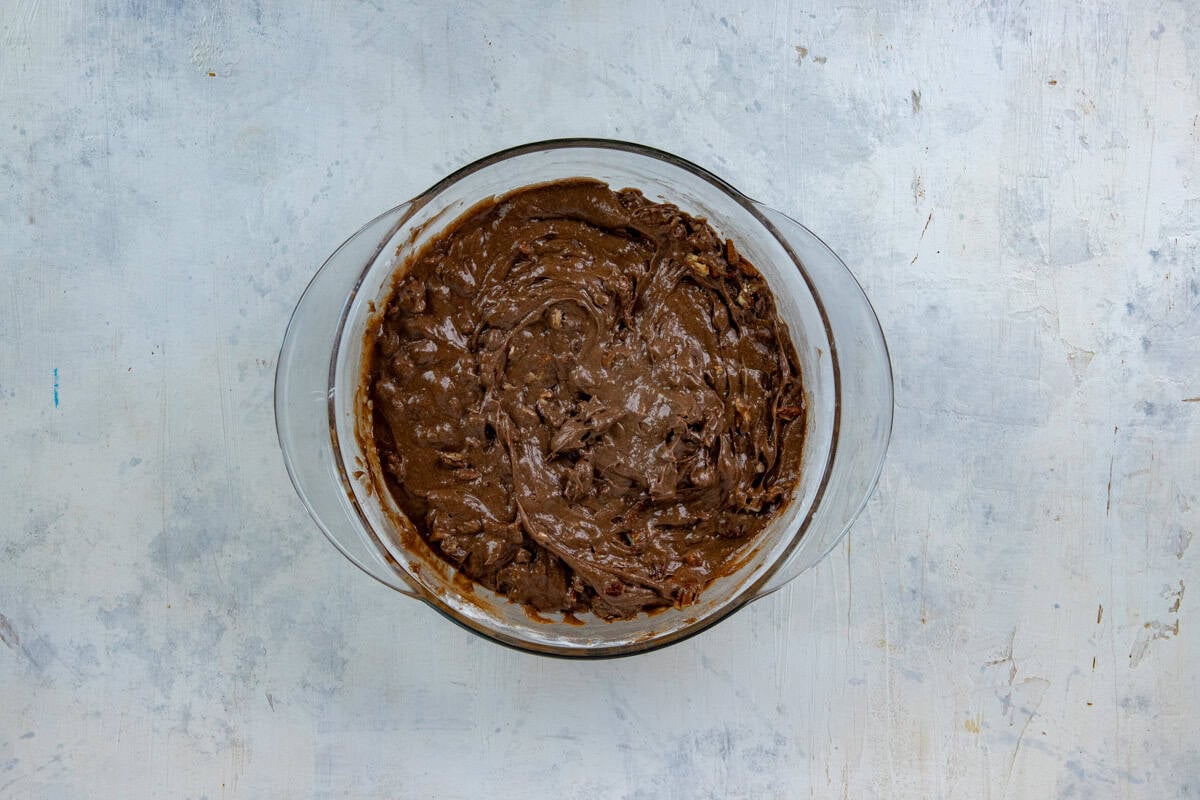 Flour, chopped pecans, and cocoa powder add to the butter mixture in a glass mixing bowl.