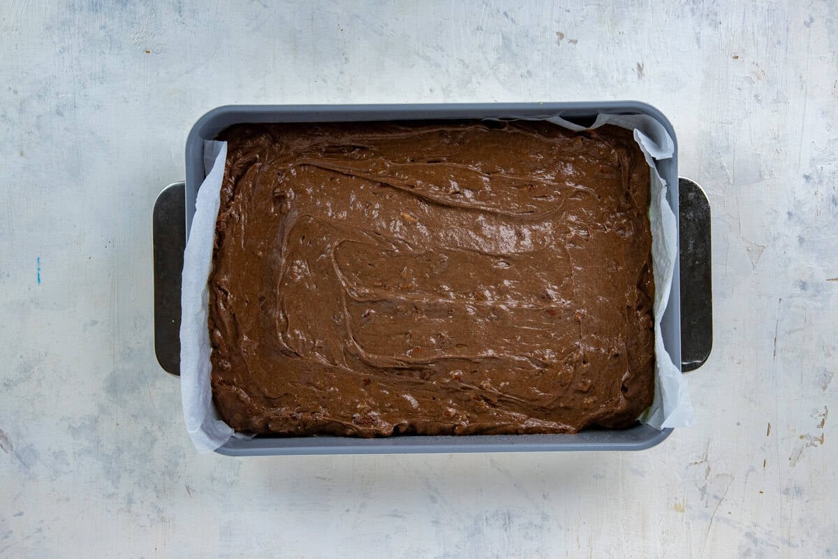 Cake batter poured into a 9-by-13-inch cake pan lined with parchment paper.