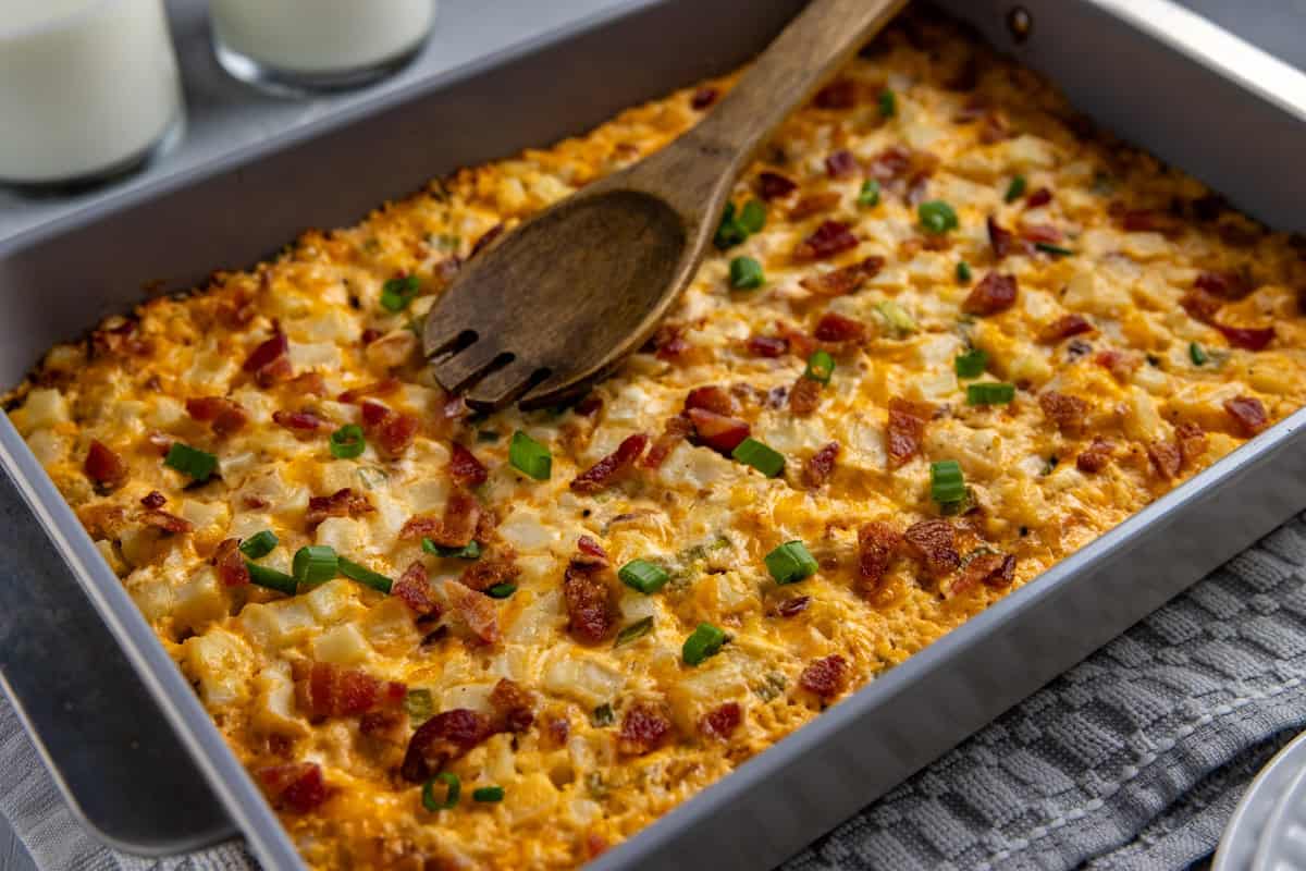Baked hashbrown casserole in the casserole dish with wooden serving spoon resting on top.
