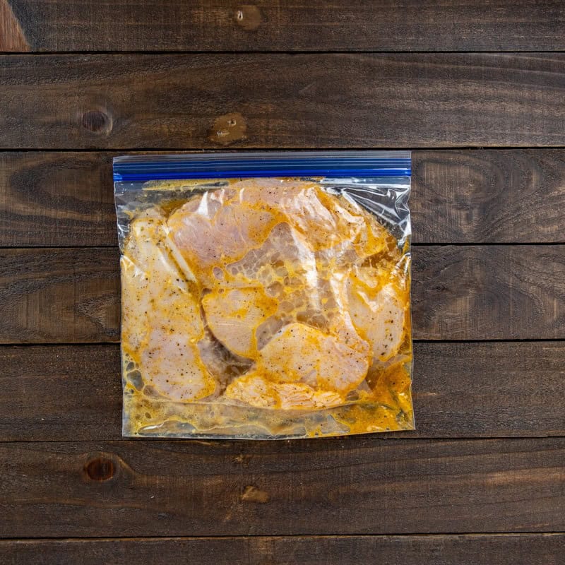 Four chicken breasts marinating in a ziptop bag.