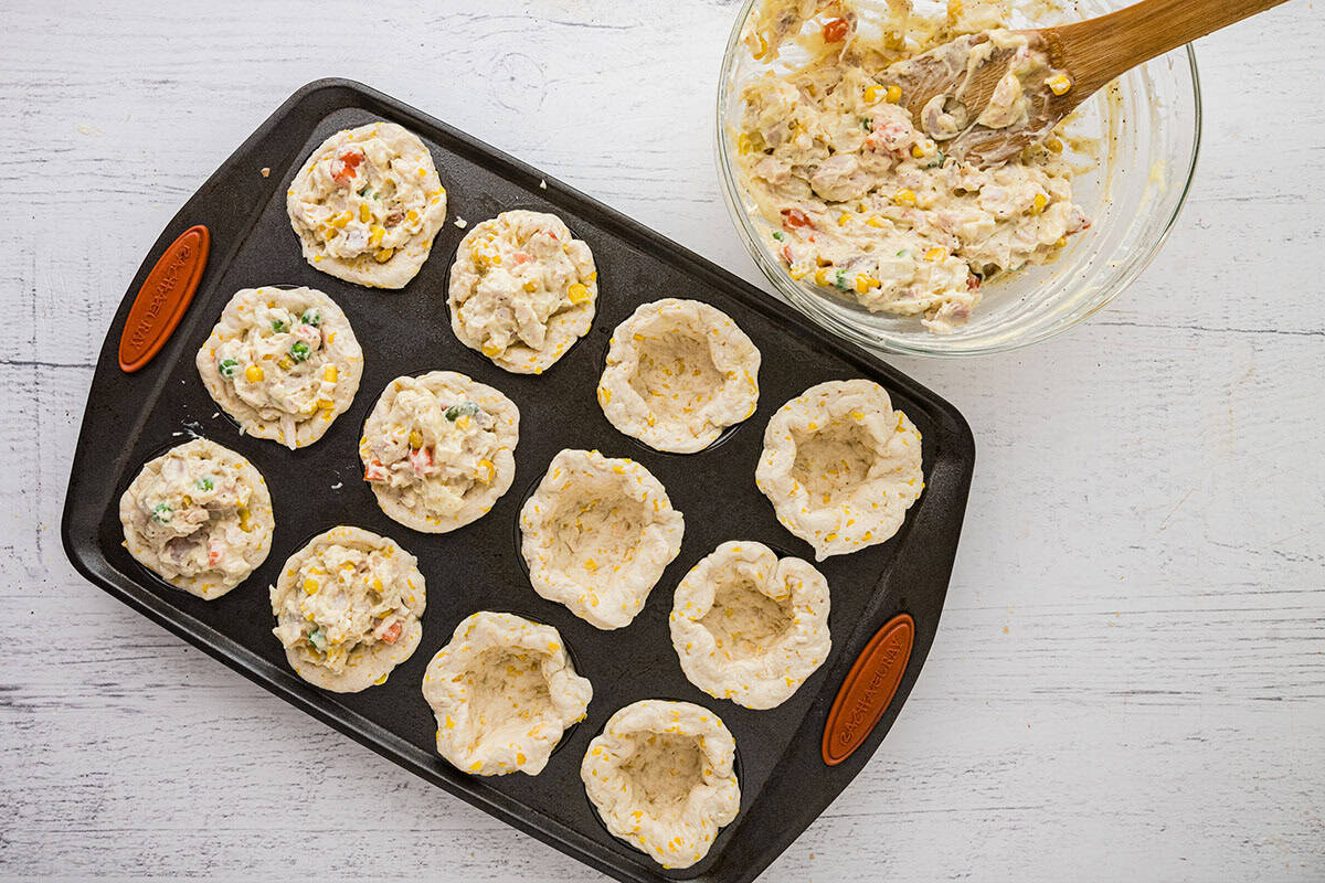 Six of the biscuits in the muffin pan filled with chicken mixture; six not yet filled.