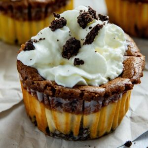 One baked nutella cheesecake cup still in the paper muffin liner topped with whipped topping and crumbled Oreos.