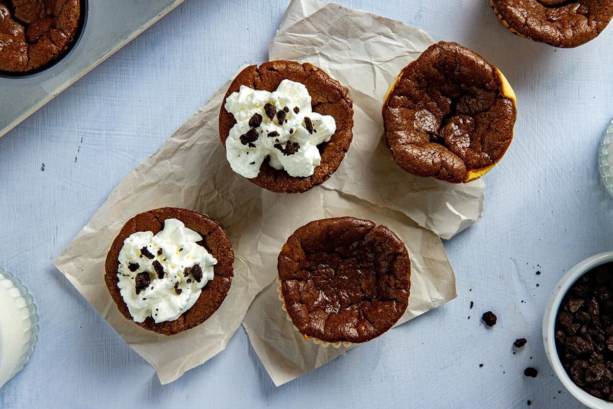Four baked Mini Nutella Oreo Cheesecake Cups. Two plain and two with whipped topping and some crushed Oreo crumbs.