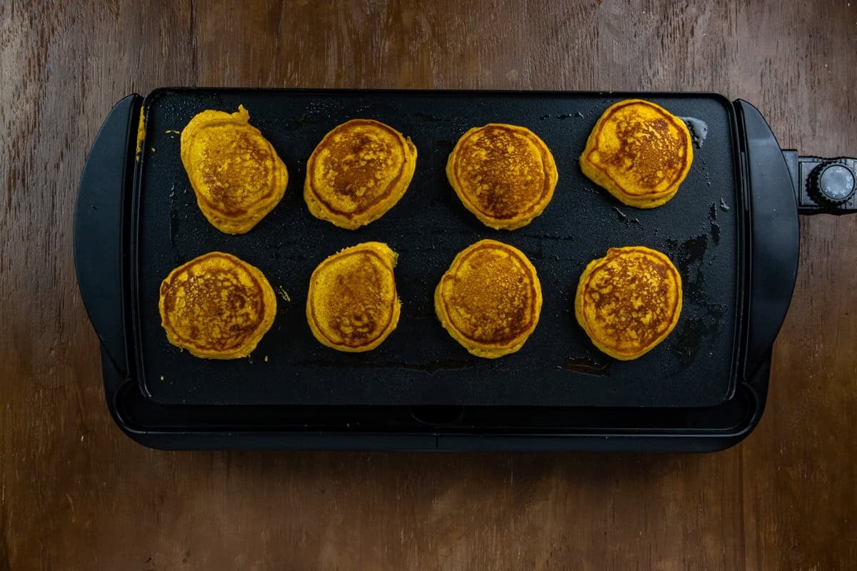 Eight cooked pancakes on a large griddle.