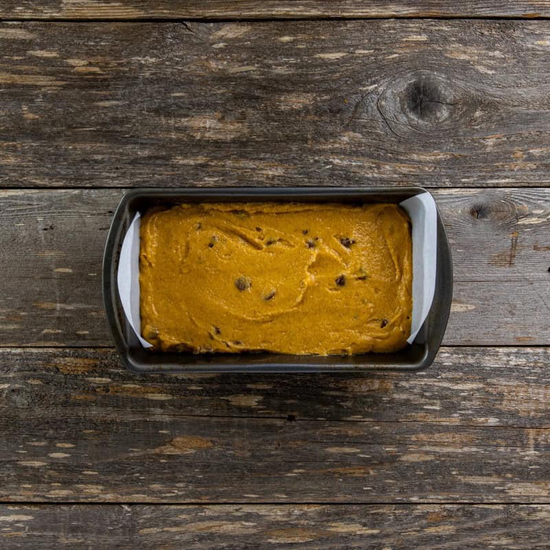 Batter poured into a 9 by 5-inch loaf pan with parchment paper handlews.