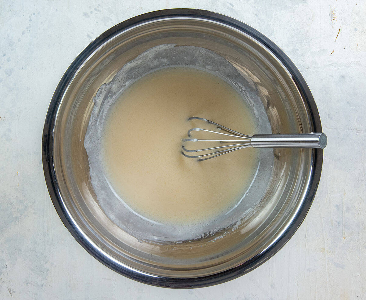 Mayonnaise, sugar, and vinegar stirred together in a bowl with a whisk.