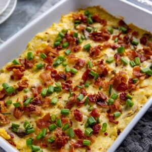 White casserole dish filled with baked mashed potatoes. Garnished with cooked crumbled bacon and sliced green onions.