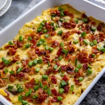 White casserole dish filled with baked mashed potatoes. Garnished with cooked crumbled bacon and sliced green onions.