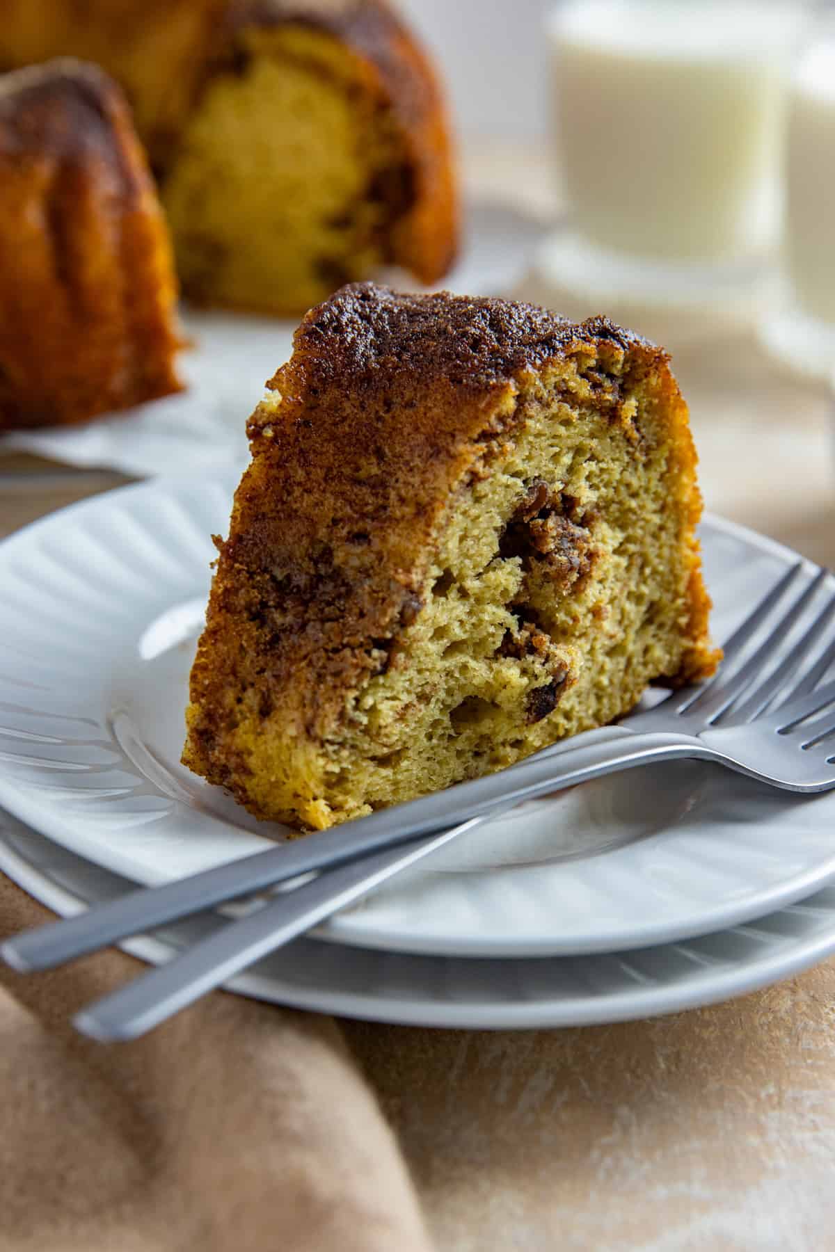 A slice of cake on top of two, stacked round white plate with two forks resting on the plate.