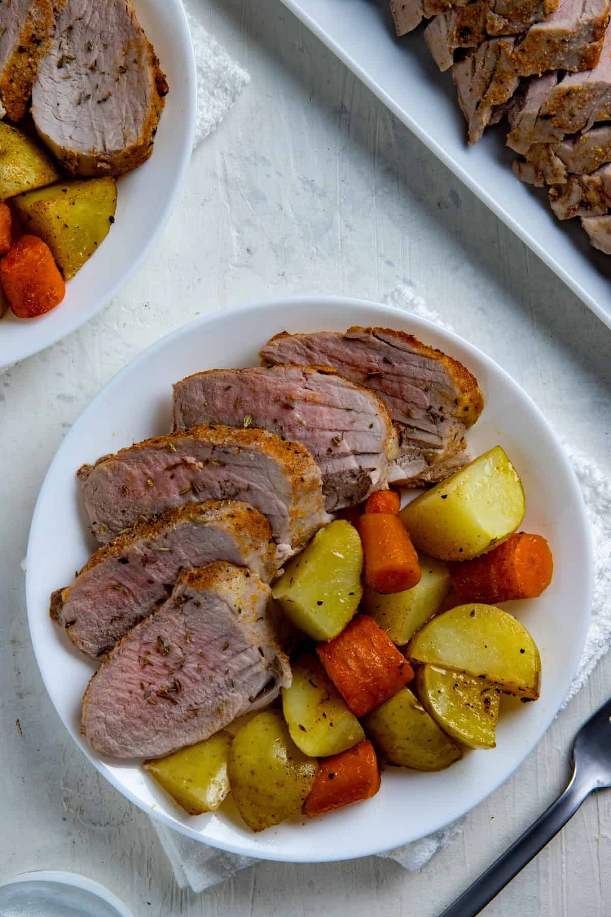 Slices of oven roasted pork tenderloin on a plate with roasted potatoes and carrots.